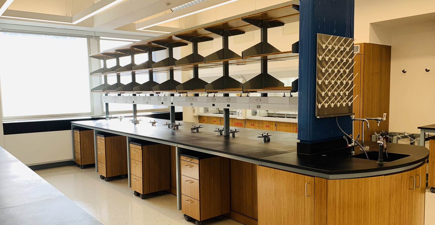 A new lab without equipment, with wooden drawers, a black counter, and blue pillar.