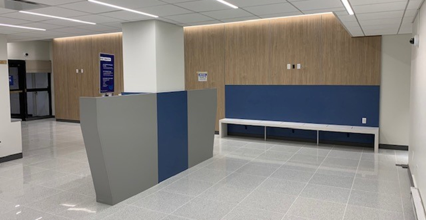 An open lobby with a grey and blue divider surroundin a thick white column, and a long bench alongside a blue and wood panel wall