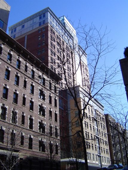 Brick apartment buildings from an upward perspective. A leafless tree partially obscures the view of the building.