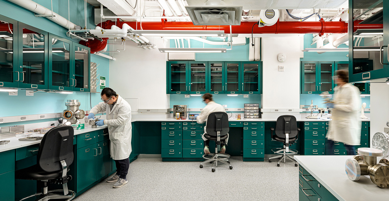 A newly renovated lab with forest green lab benches and cabinets. Three researchers are in the lab, working.