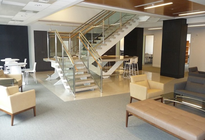Open collaboration space with white high-top tables and stools and neutral-colored lounge chairs and couches. A staircase is in the center of the space.