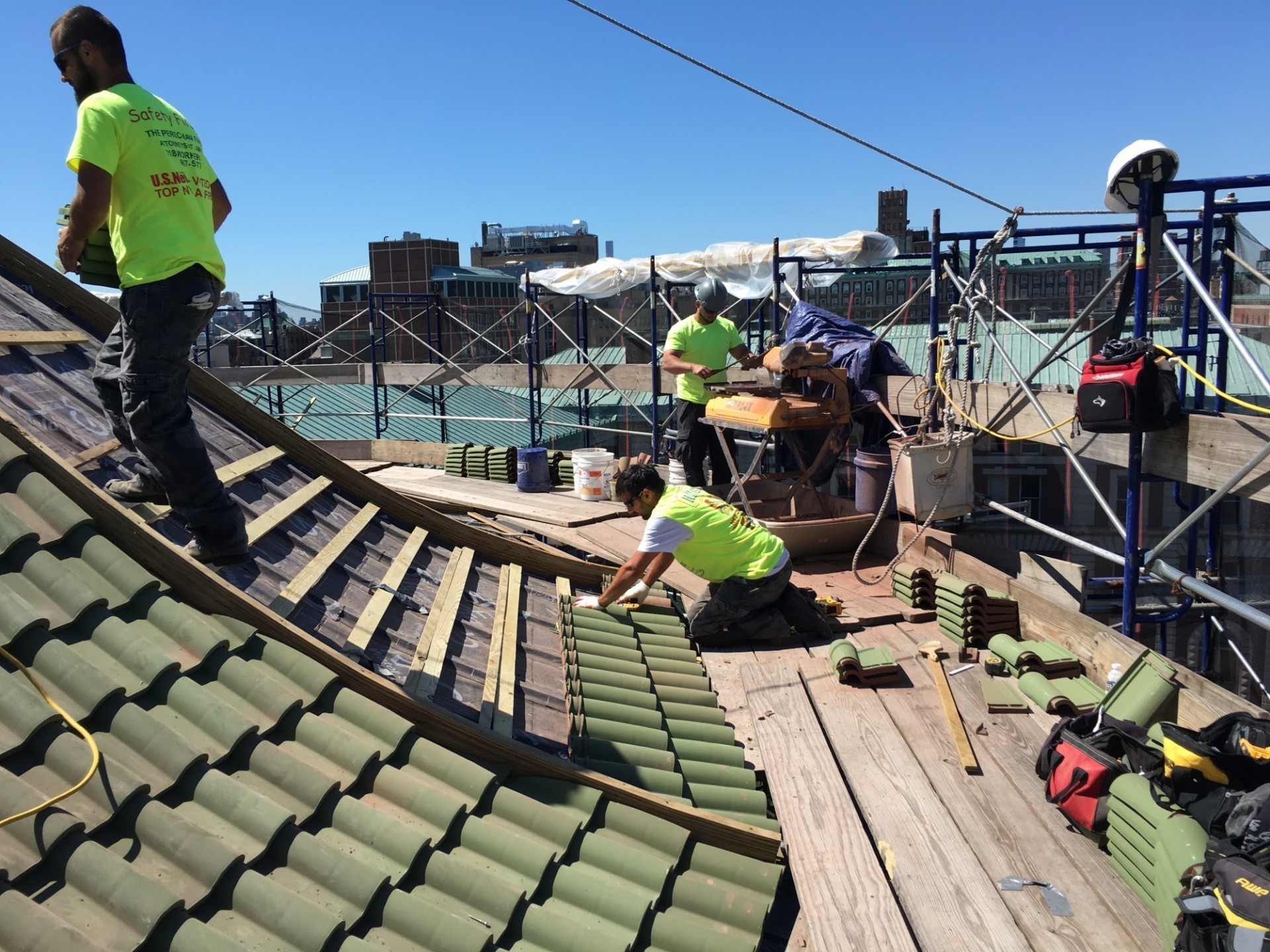 Workers replacing terra cotta roof tiles on top of the Chapel's roof during a cloudless, sunny day.