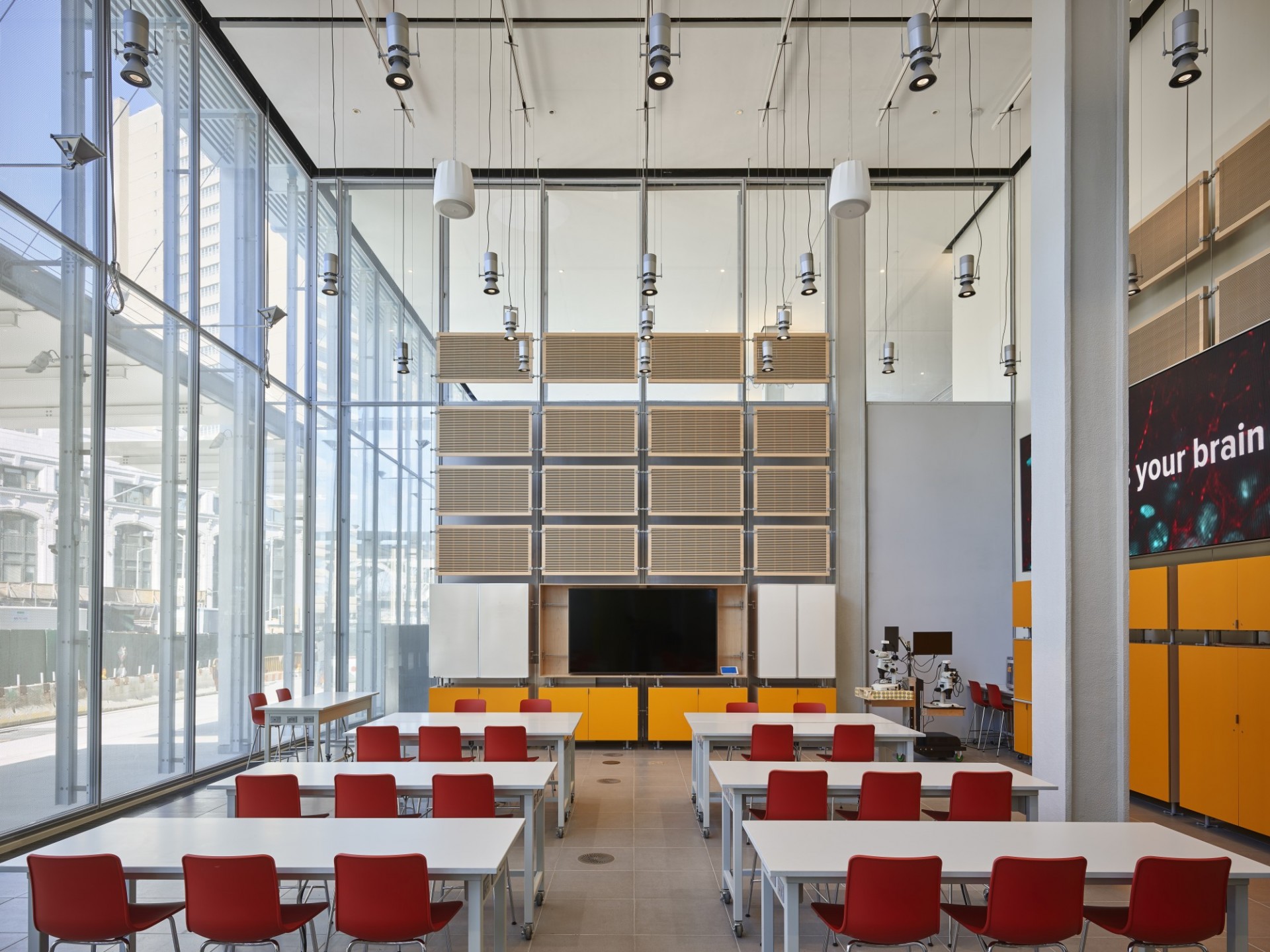 The Community Education Lab. Photo by Frank Oudeman. A classroom in the JLG Science Center with rows of red chairs at white, bench-style tables facing a TV monitor.