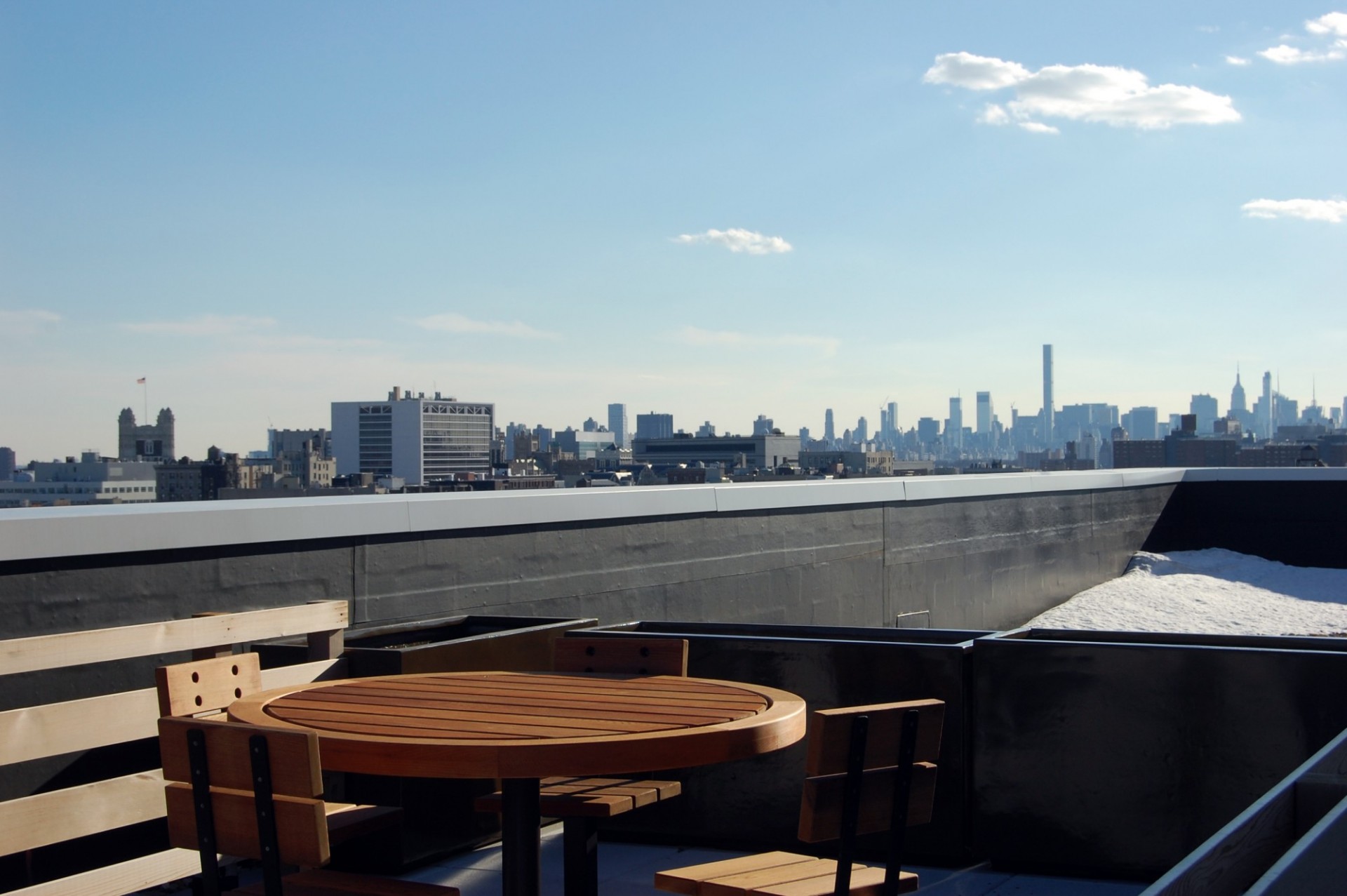 A round wooden table and chairs on the rooftop of 3595 Broadway with the Manhattan skyline in background.