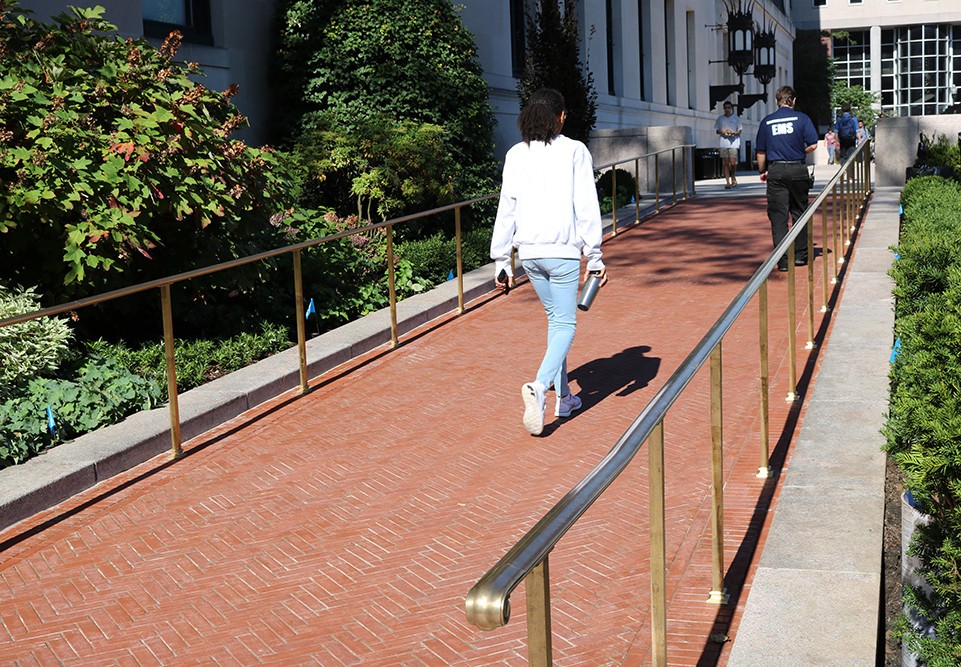 A person walks up the red brick paver ramp. They are wearing a grey sweatshirt and blue jeans. 