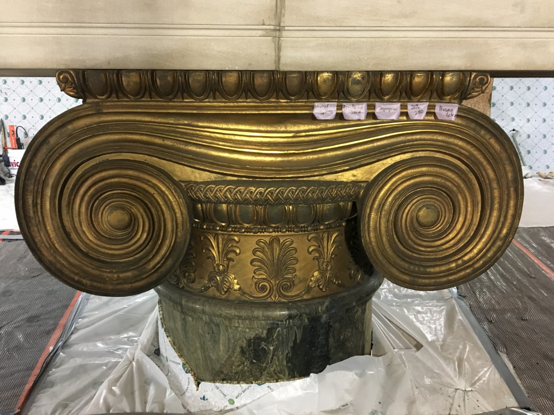 A gilded bronze column capital with tape labels marking sections.