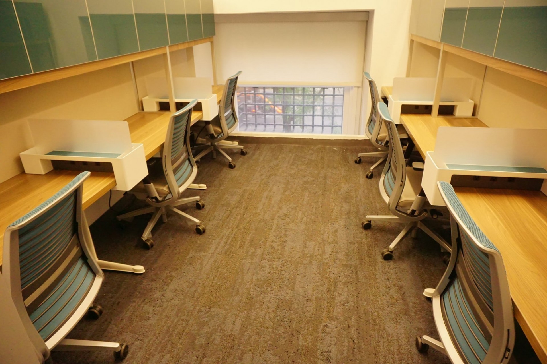 There are six workstations, three on either side of the room. Each station is divided by a frosted glass partition and has a light blue office chair.