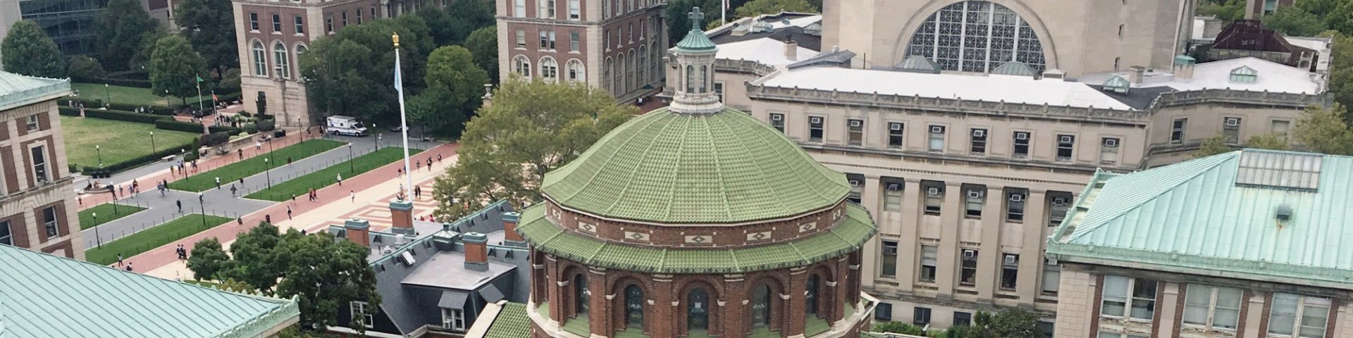 Aerial view of St. Paul's Chapel, a red brick building with a green, terra cotta tile roof, and campus. Historic stone buildings surround the chapel. Green lawns and red brick paver walkway in the background.