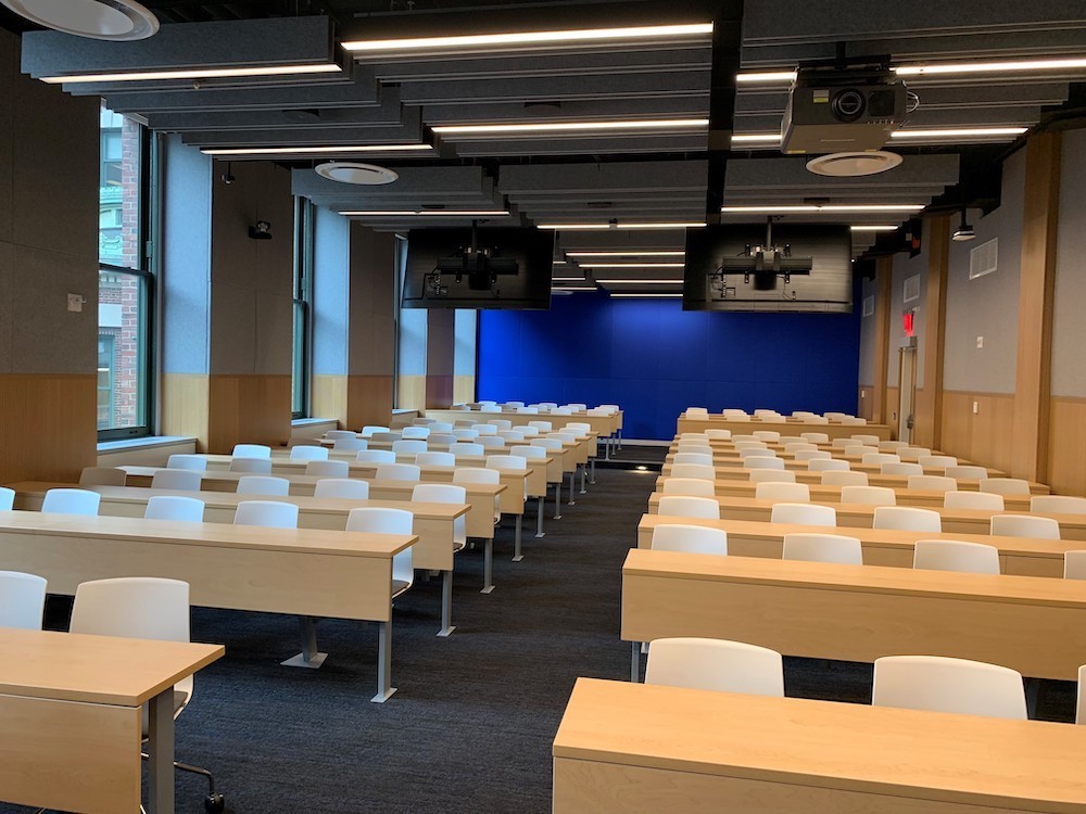 Rows of long wooden tables with white plastic chairs