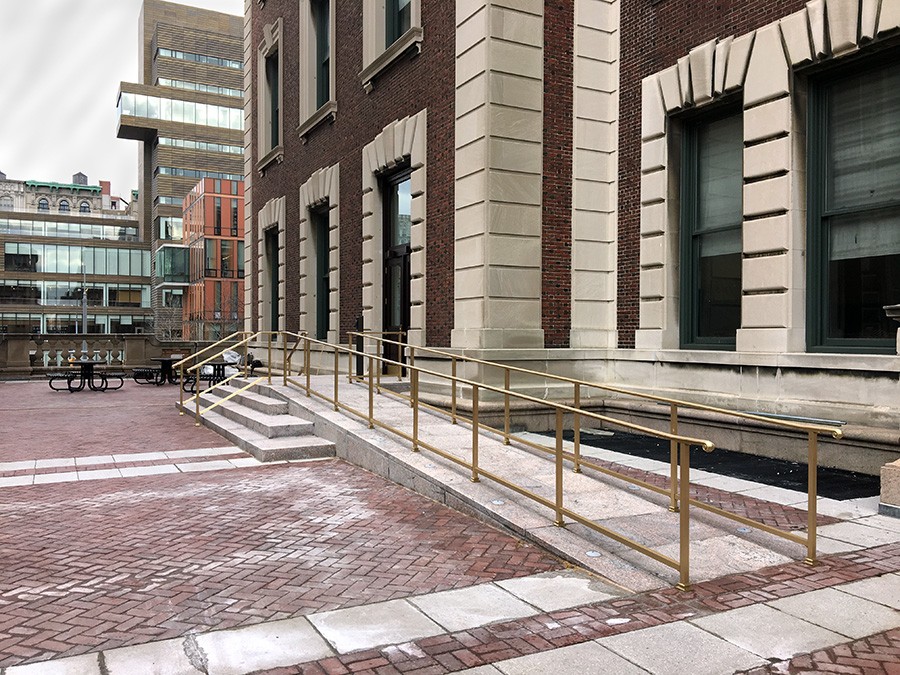 Concrete ramp with gold railings on either side provides accessible entrance to a brick academic building.