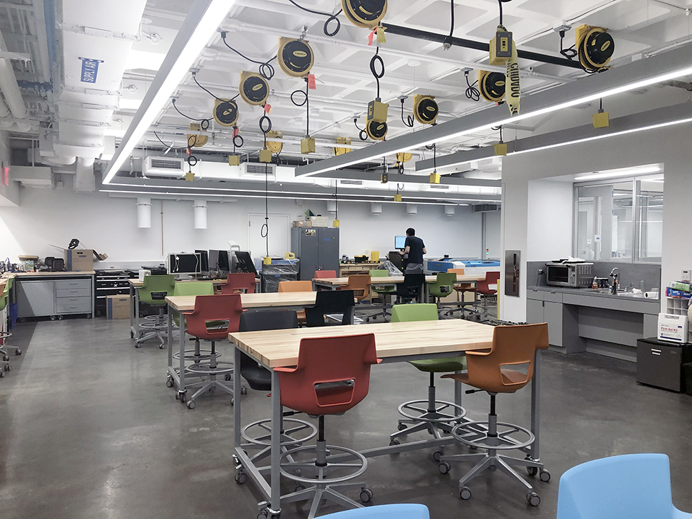 Open work space with wooden lab tables and multi-color stools. 