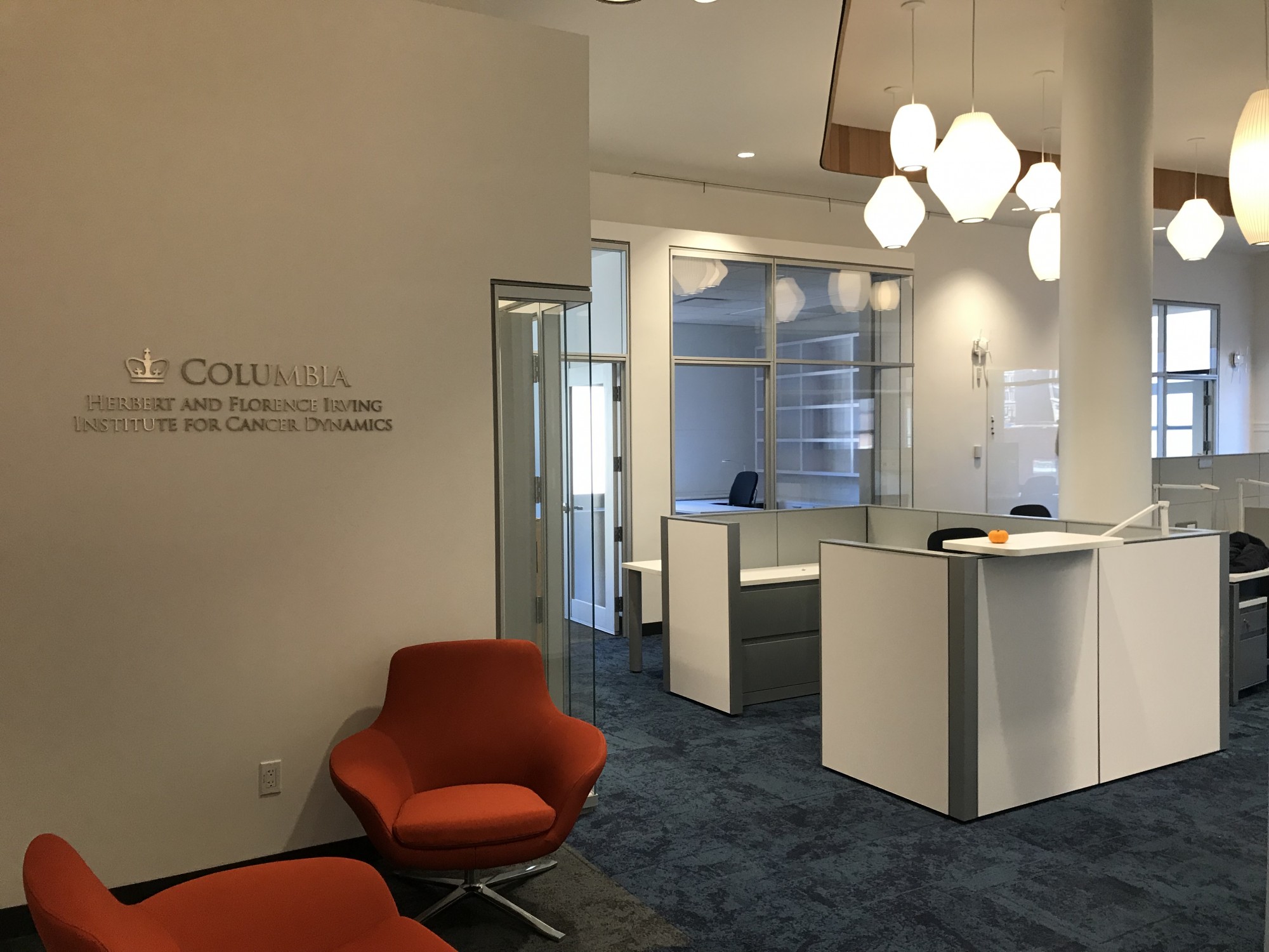 White-walled office space with white work cubicles and two orange sitting chairs. 