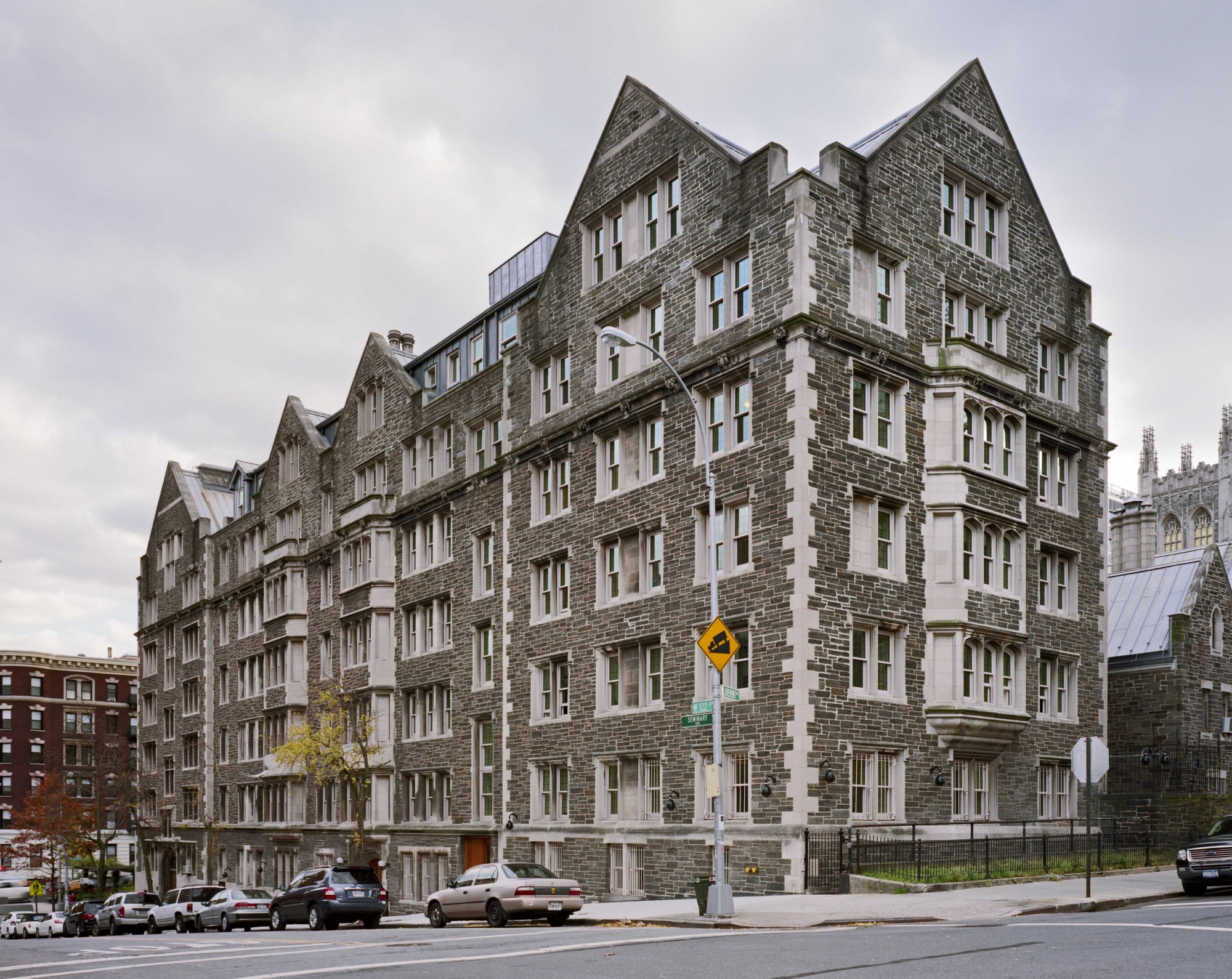 Seven-story stone building at the corner of two streets against a cloudy grey sky.