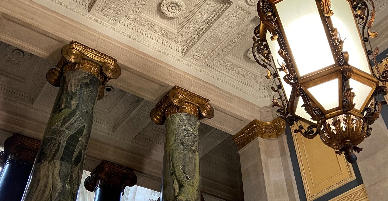 View of Low Library ceiling. The ceiling is white with an ornate pattern. A lantern-like chandelier hangs from the ceiling center.