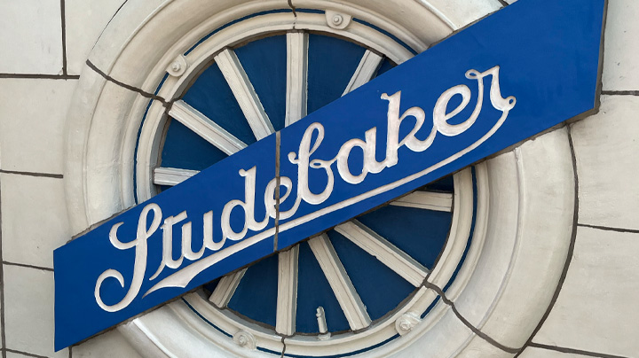 An ivory wheel that has a blue sign across it that says, "Studebaker" against ivory tile facade.