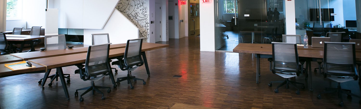 Open collaborative space with long wooden tables and wood floor.