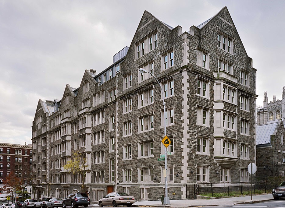 Grey stone building at the corner of two streets with cloudy sky in background.