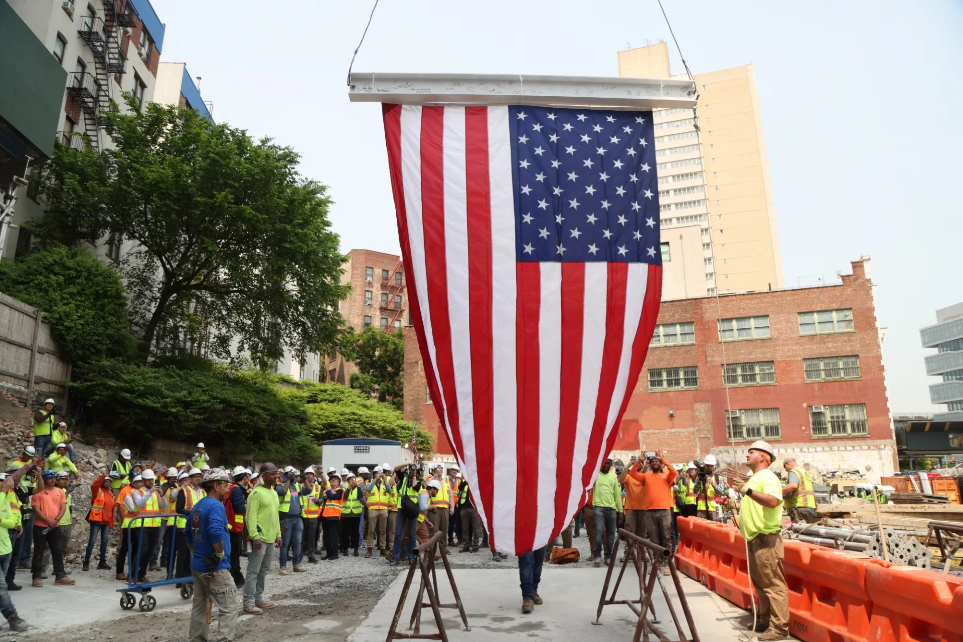 A steel beam with a flag attached to it is hoisted above a crowd.