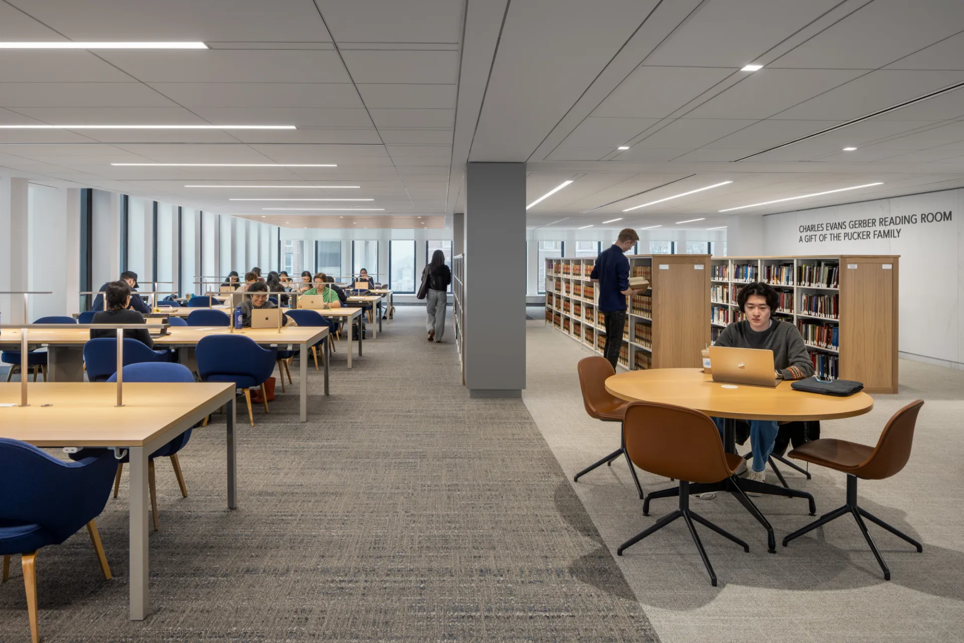 The Gerber Reading Room, featuring long tables and blue chairs, a round table, and stacks of bookshelves with books.