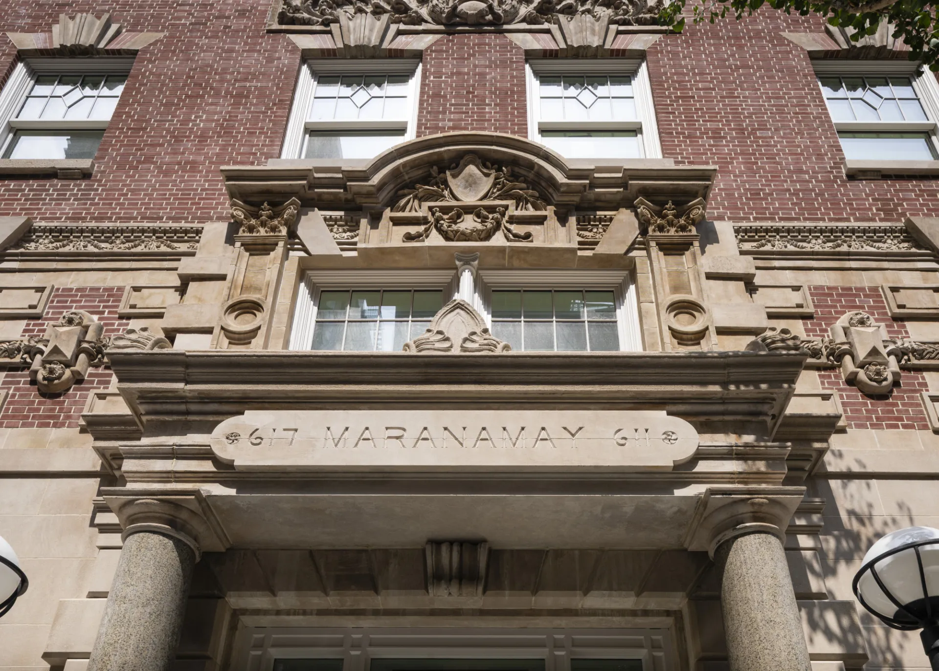 A view looking up from the entryway of 611 W. 112th Street, which has ornate features above the entrance, and red brick on the upper floors.