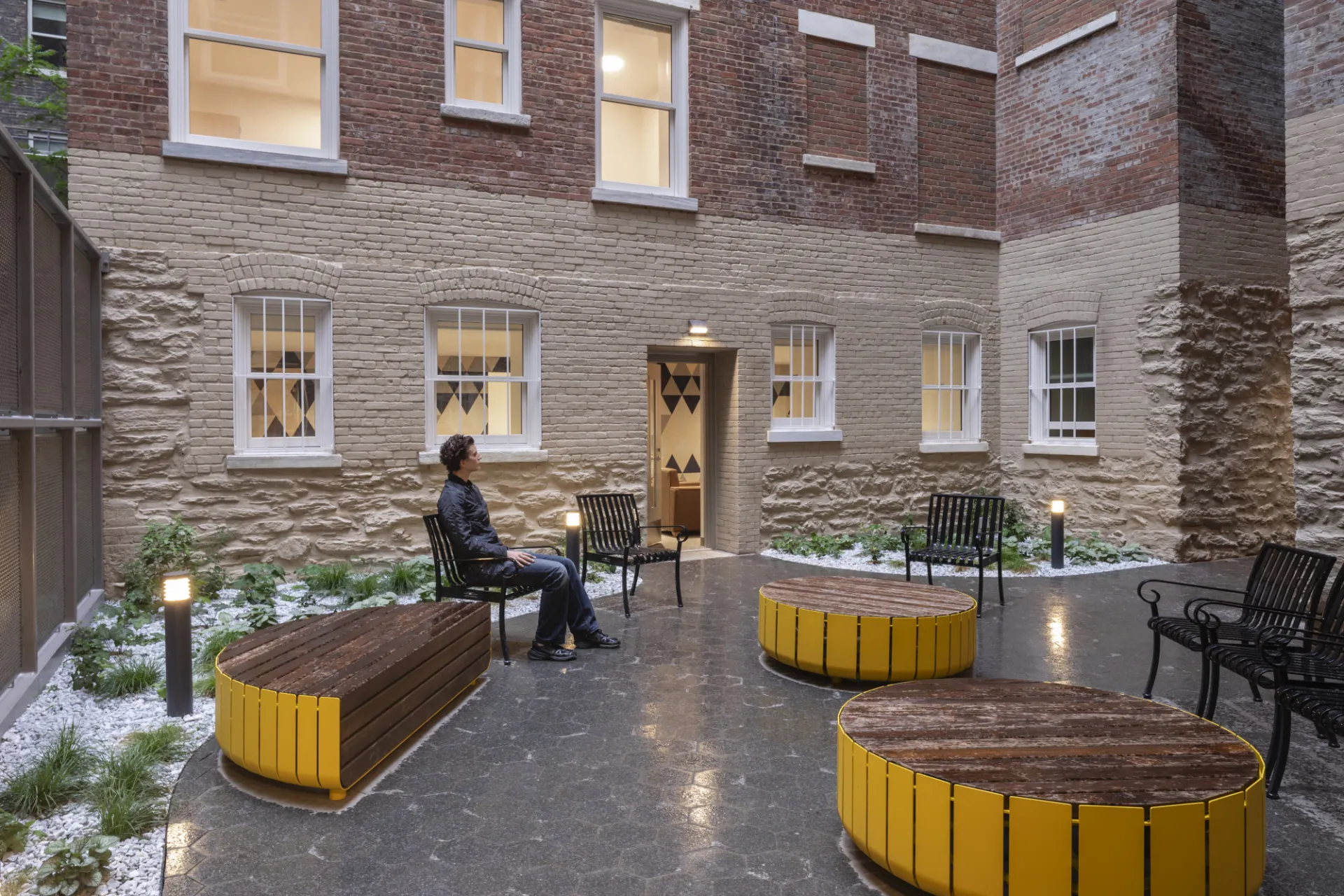 A student sits on a chair at one of the courtyards in 611 W. 112th Street, which has wood benches and ottomans with yellow accents.