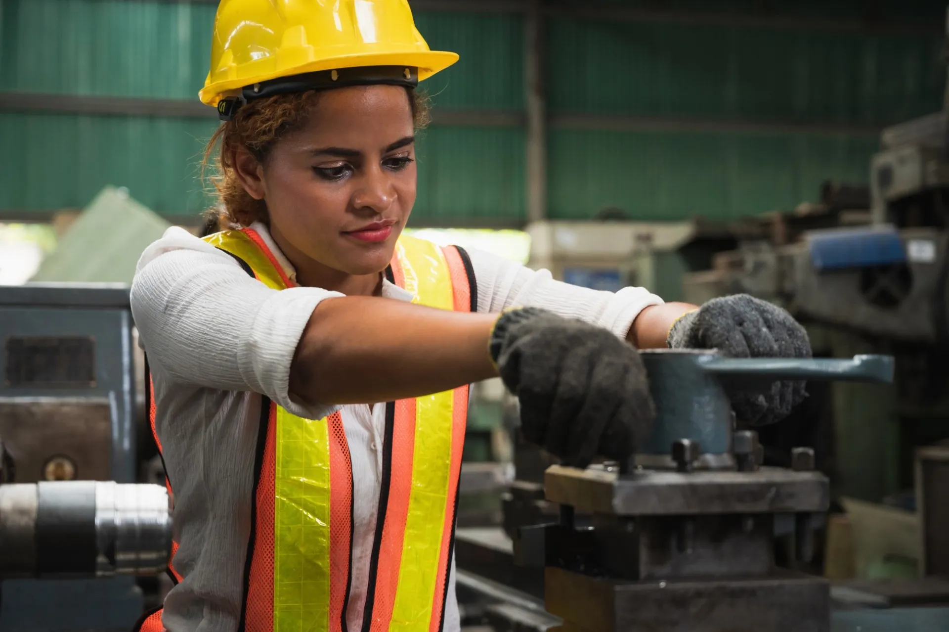 A person wearing a construction hat and a reflective vest is working with some machinery inside of a construction site