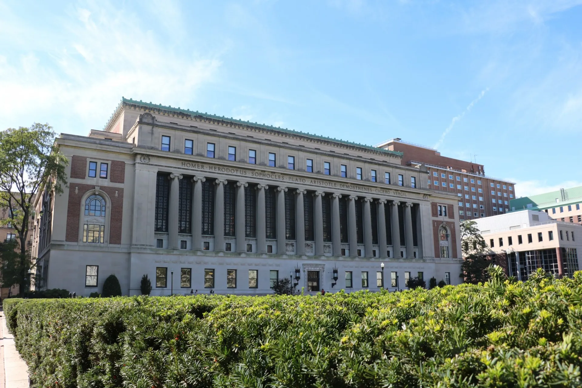 A view of Butler Library behind hedges on a sunny day.