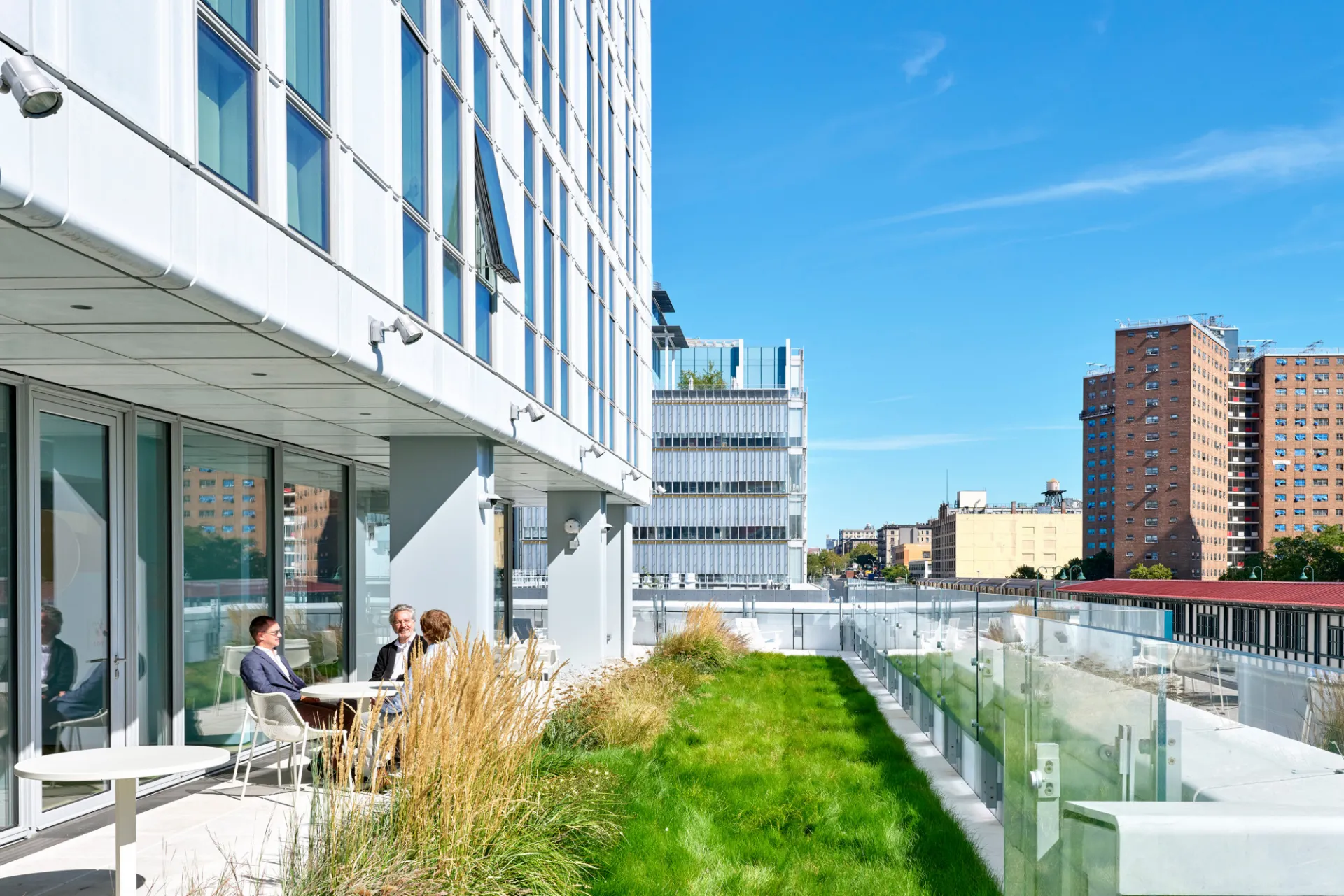 Residents sit at a table on a landscaped terrace at 600 W. 125th street, with Jerome L. Greene Science Center in the background.