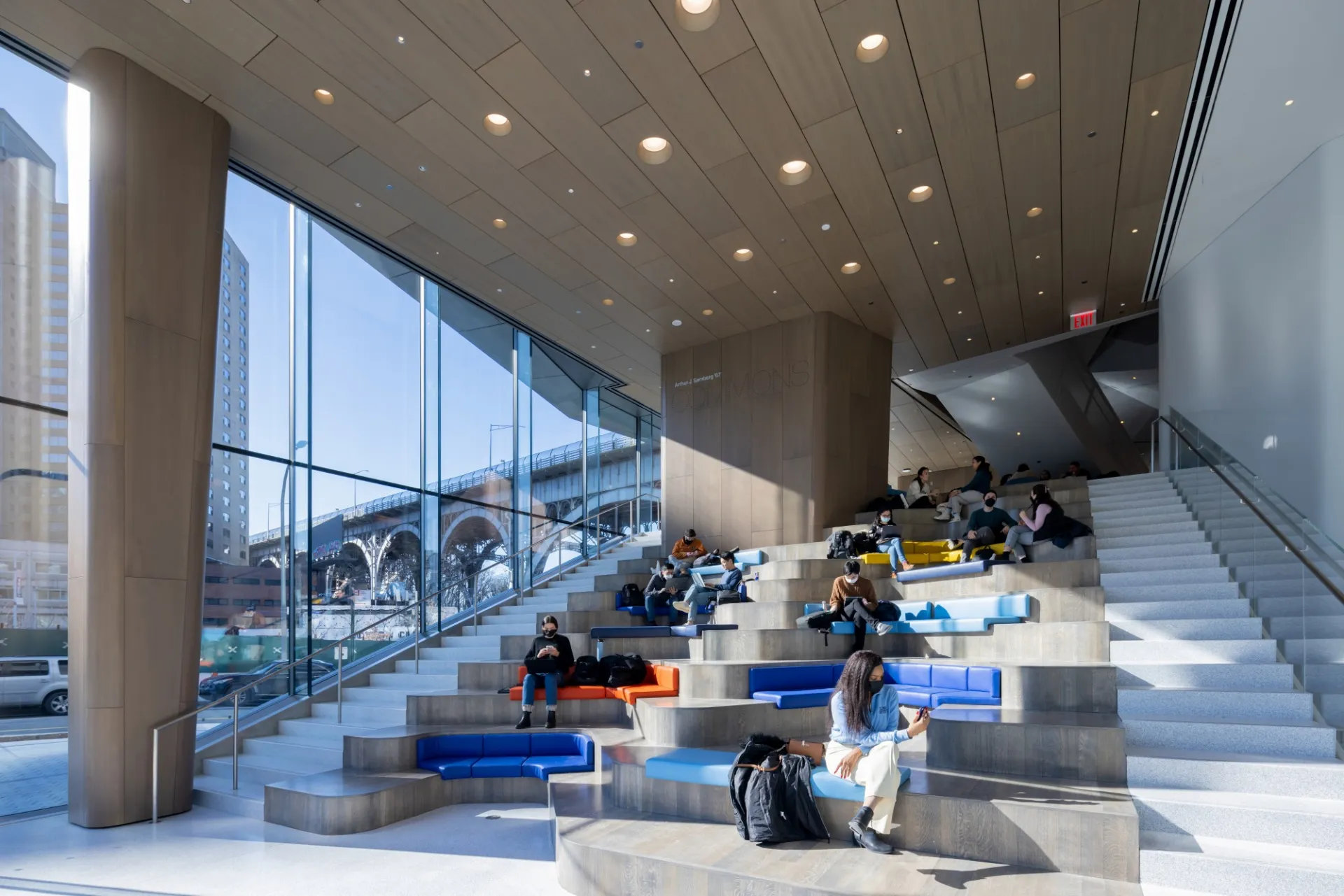 A group of students sit on the steps of the Samberg Commons, with the Viaduct visable from the side windows.