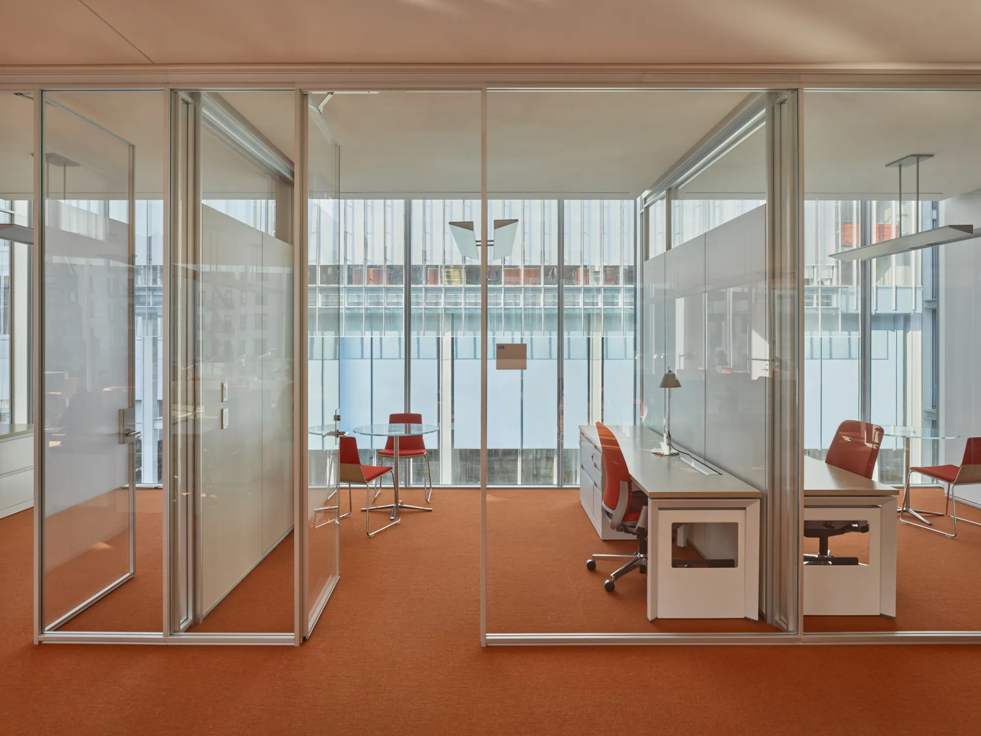 Private, glass-walled meeting spaces furnished with a desk and glass table.