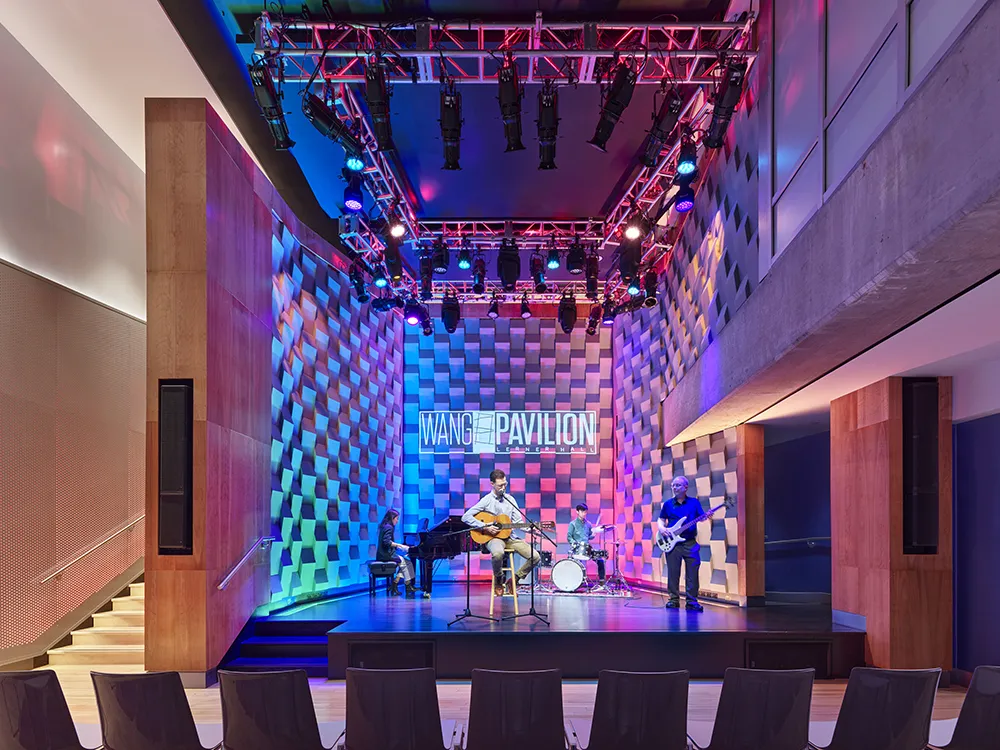 A jazz trio jams out on the stage of the Wang Pavilion, which has purple and pink lights illuminating the wall behind them.