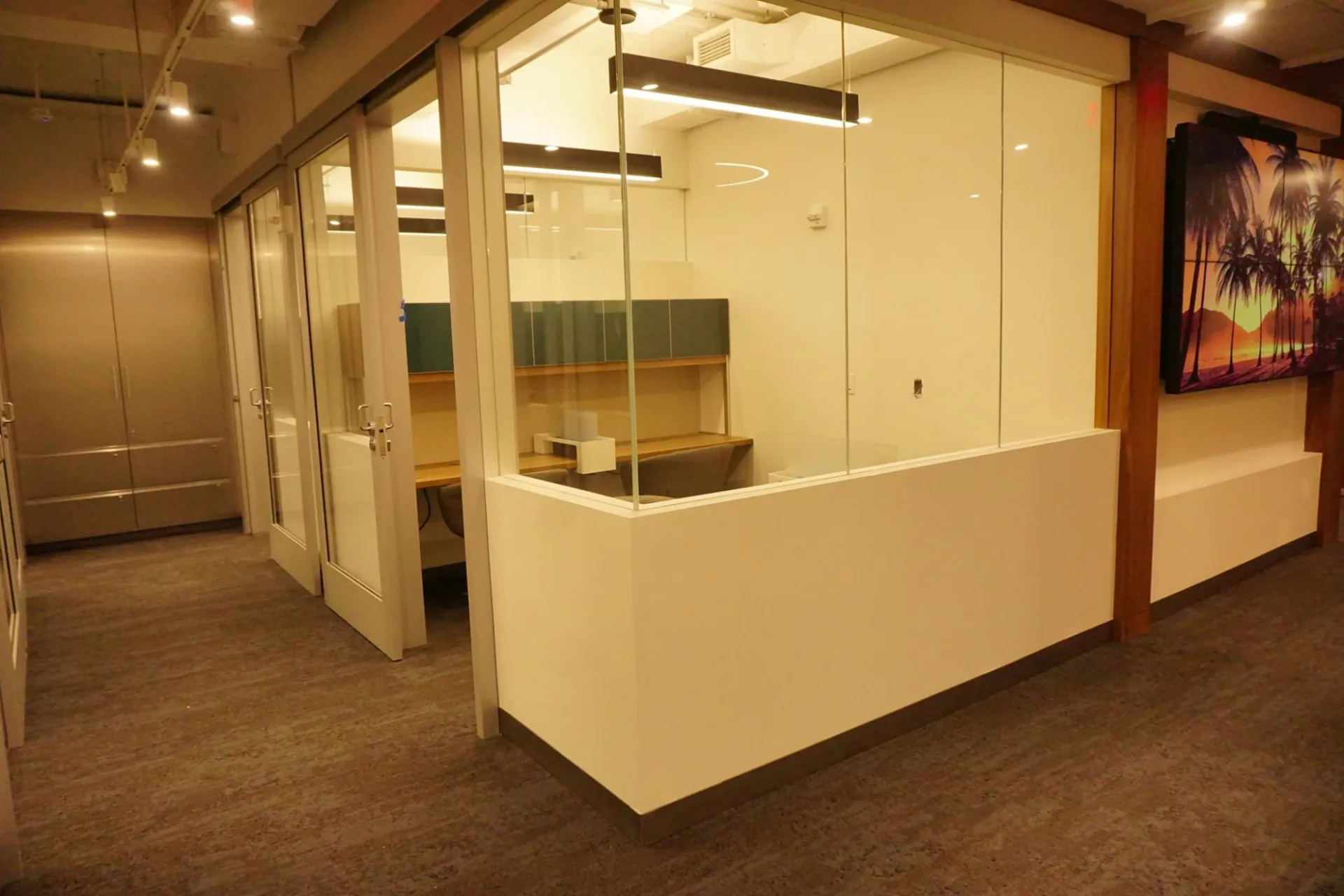 A room sits at the corner of two hallways. The rooms' walls are half glass window and half white plaster.