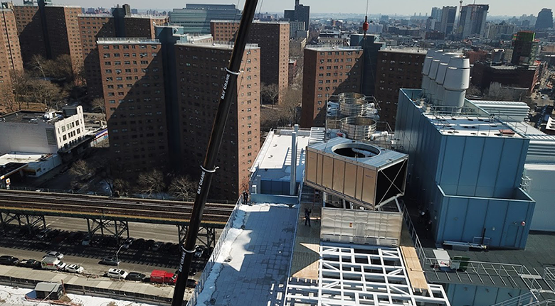 A crane is lowering a large cooling unit onto the roof a building.